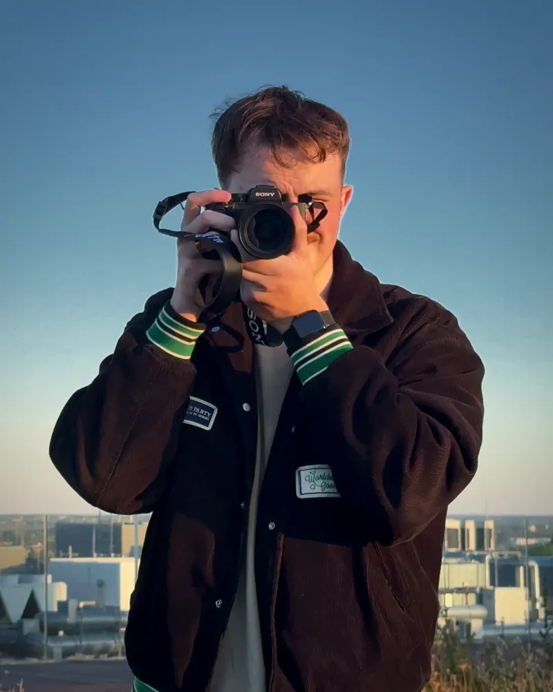 Jakub Rola, fotograf z Lublin, patrzy przez wizjer aparatu na dachu z widokiem na miasto